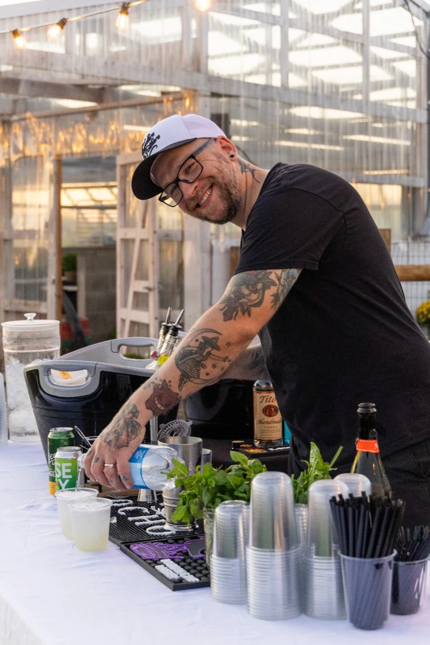 A bartender preparing a cocktail beneath warm string lights